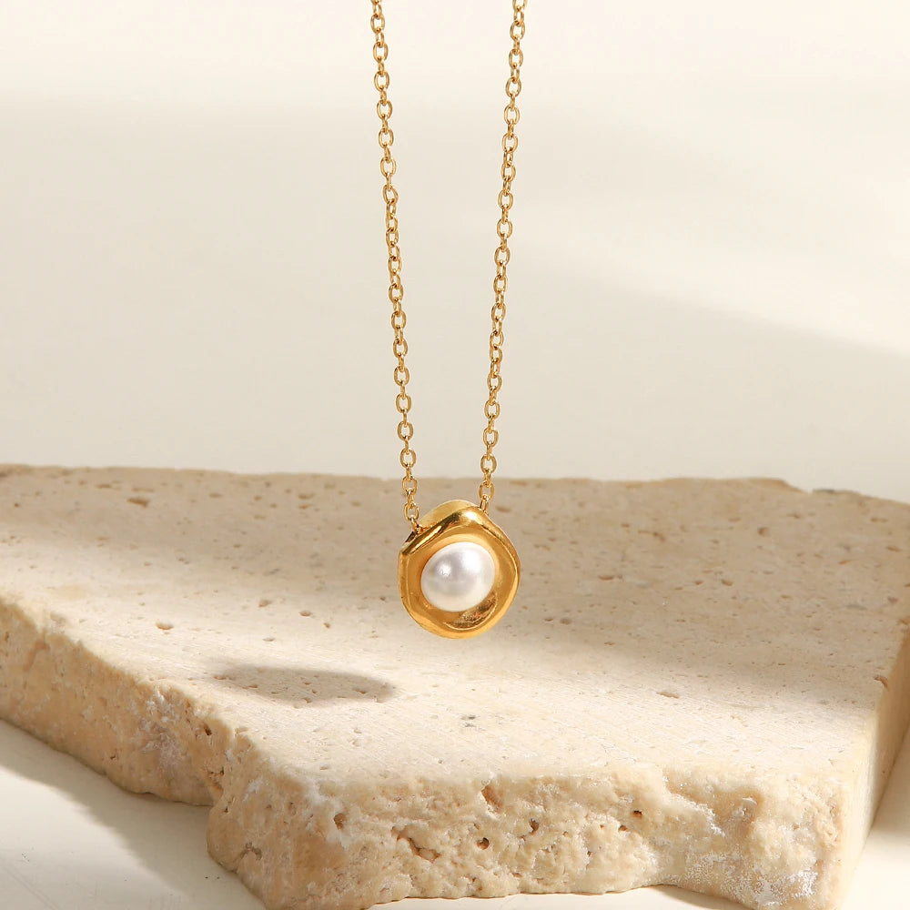 Gold necklace with a pearl pendant on a beige stone surface
