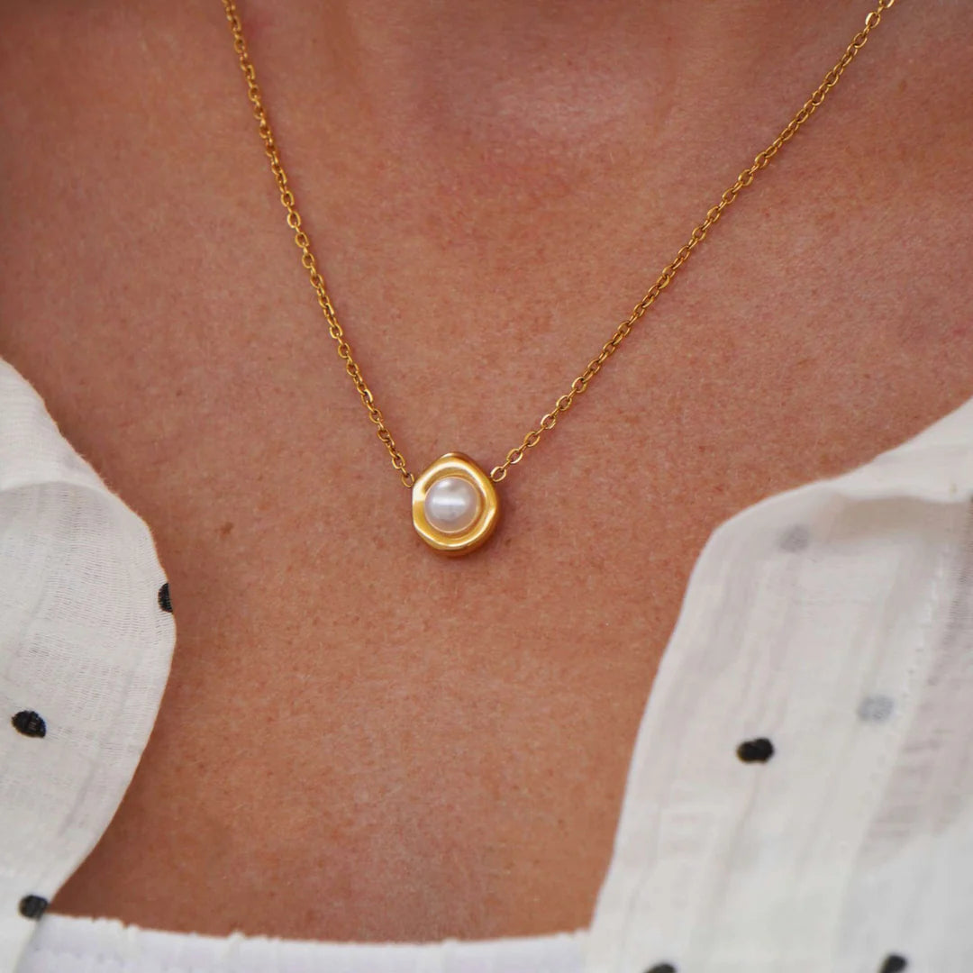 Gold necklace with a pearl pendant on a person wearing a white blouse.
